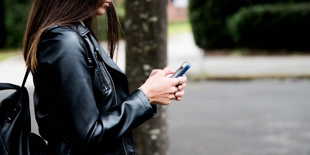 A woman using her phone while walking down the street.